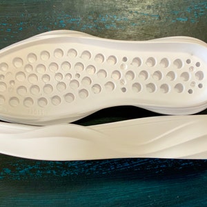 May include: Two white shoe soles, one with a textured surface and the other with a wavy design.