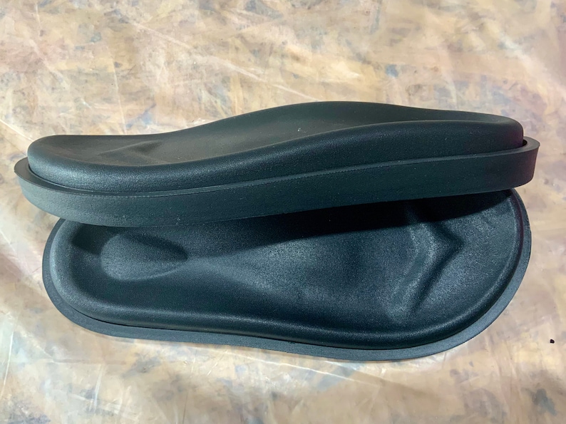 May include: Two black foam footbeds for sandals or slippers. The footbeds are curved and have a raised edge around the perimeter.