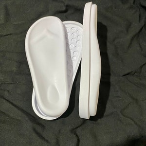 May include: Two white plastic foot molds for making custom orthotics. The molds are designed to fit the shape of the foot and are used to create custom orthotics that can help to relieve pain and improve comfort.