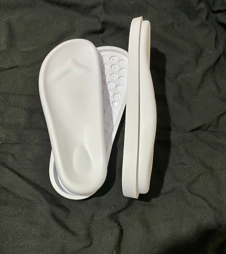 May include: Two white plastic foot molds for making custom orthotics. The molds are designed to fit the shape of the foot and are used to create custom orthotics that can help to relieve pain and improve comfort.