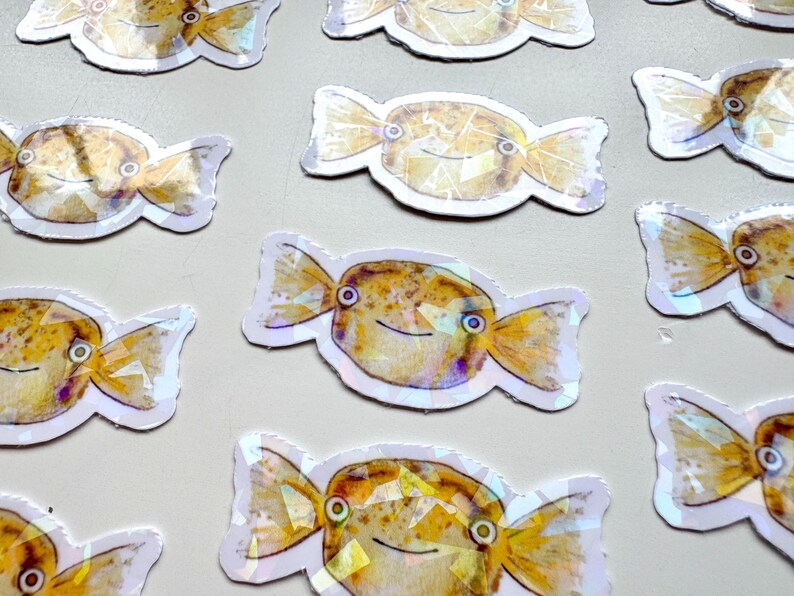 May include: A set of ten colorful, iridescent stickers featuring a cartoon fish shaped like a candy. The fish have yellow bodies with brown spots and black eyes. The stickers are perfect for adding a whimsical touch to laptops, water bottles, or journals.