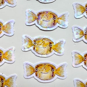May include: A set of 10 iridescent stickers featuring a cartoon pufferfish with a candy-like design. The stickers are white with a holographic finish and feature a yellow and brown pufferfish with black eyes and a smile.