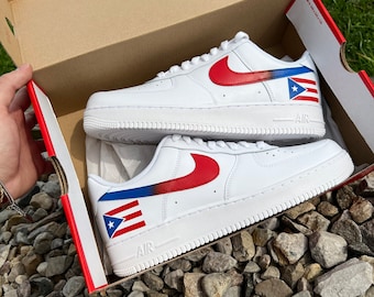 May include: White leather sneakers with a red swoosh and a Puerto Rican flag design on the side. The sneakers are in a cardboard box.