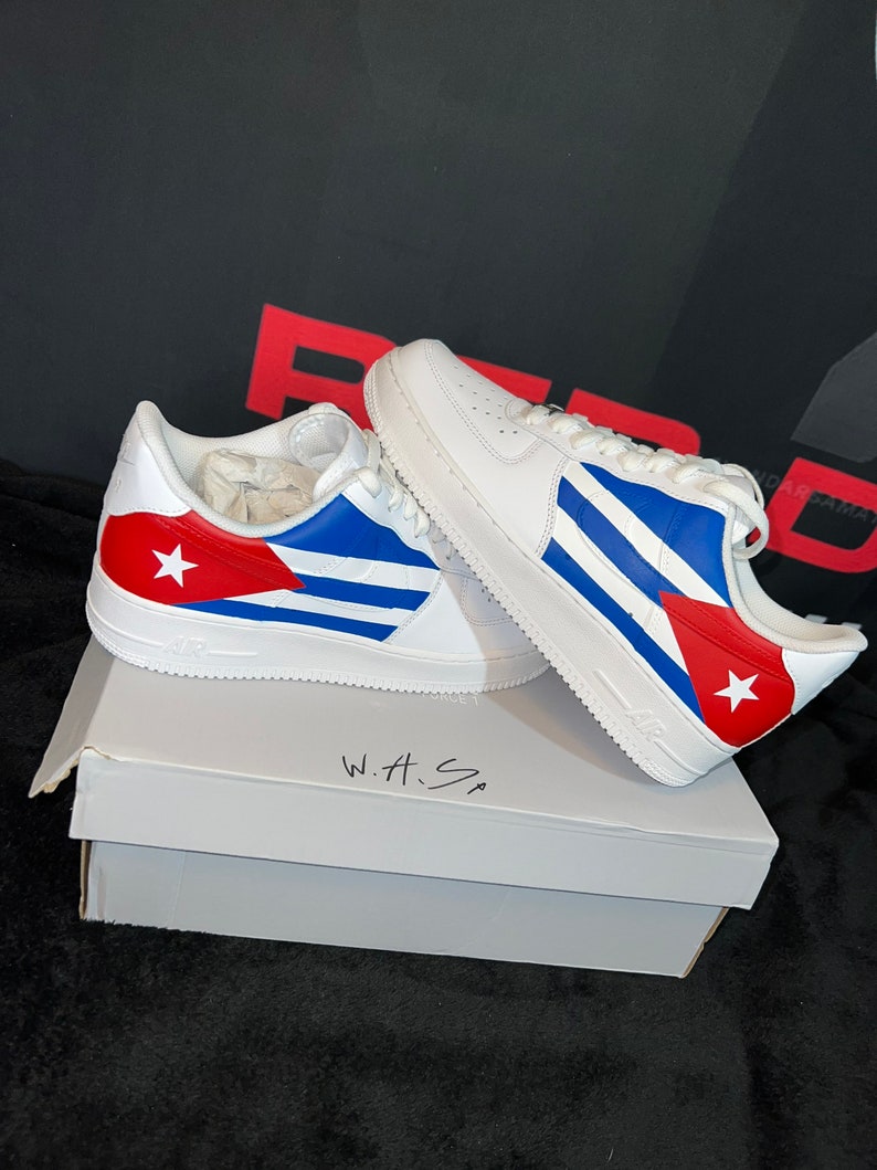 May include: White sneakers with a Cuban flag design. The sneakers are sitting on a white box with the words "W.H.S" written on it.
