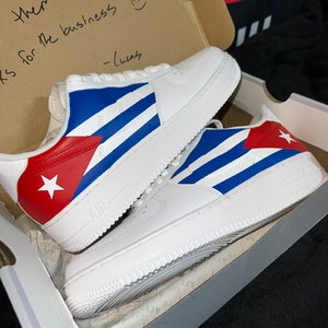 May include: A pair of white sneakers with a custom design featuring the Cuban flag colors: red, white, and blue. The sneakers are in a shoebox with a handwritten note that says "I like them! Thanks for the business - Chels"