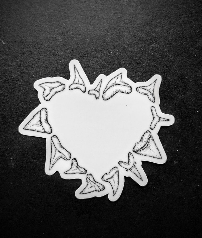 May include: A white sticker in the shape of a heart, outlined with black shark teeth. The teeth are detailed with small black dots, creating a textured effect. The sticker is on a black background.