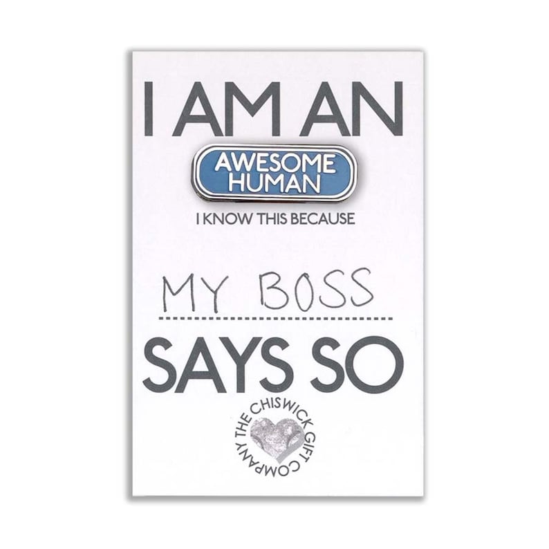 May include: A white card with the text "I am an Awesome Human. I know this because my boss says so."  The card features a blue enamel pin with the text "Awesome Human" in white. The card is from The Chiswick Gift Company.