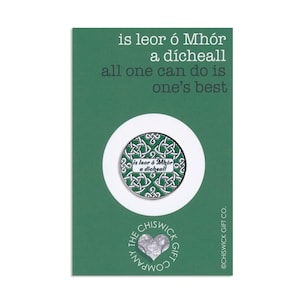 Könnte beinhalten: Eine grüne Karte mit dem Text "is leor ó Mhór a dícheall all one can do is one's best". Die Karte zeigt eine runde Anstecknadel mit keltischem Knotenmuster und dem Text "is leor ó Mhór a dícheall". Das Logo von Chiswick Gift Co. befindet sich unten.