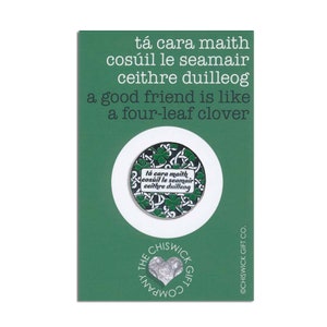 May include: A green and white enamel pin with a four-leaf clover design. The pin features the Irish phrase "tá cara maith cosúil le seamair ceithre duilleog" which translates to "A good friend is like a four-leaf clover".
