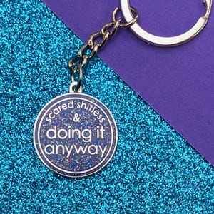 May include: A silver keyring with a round, iridescent charm that says "scared shitless & doing it anyway".