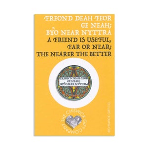 May include: A yellow card with a green, orange, and yellow enamel pin featuring a Welsh proverb in black text: "Freond deah feor ge neah; Byo near nyttira." The text translates to "A friend is useful, far or near; the nearer the better." The card also features the text "The Chiswick Gift Company" in a silver heart shape.