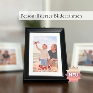 Könnte beinhalten: Ein schwarzer Bilderrahmen mit einem Foto von Vater und Kind am Strand. Das Wort "Papa" ist in roter Schrift geschrieben. Der Text "Personalisiert Bilderrahmen" befindet sich über dem Rahmen.