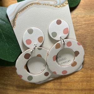 May include: A pair of white hoop earrings with a brown, green, and pink polka dot pattern. The earrings are on a card with the text "Han Gbird Jewelry".