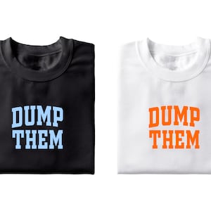 Könnte beinhalten: Zwei gefaltete T-Shirts mit dem Aufdruck "DUMP THEM" auf der Vorderseite. Das T-Shirt links ist schwarz mit hellblauem Text. Das T-Shirt rechts ist weiß mit orangefarbenem Text.