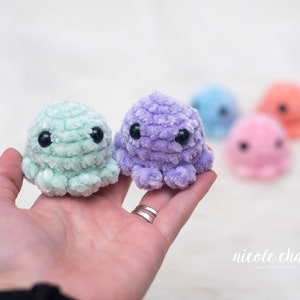 May include: A pair of handmade crochet octopus toys in mint green and lavender, with black safety eyes. Several other colorful octopuses are blurred in the background. The toys are soft and plush, perfect for children.