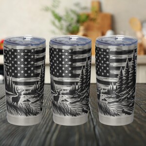 以下が含まれることがあります： アメリカの国旗、木々、鹿が描かれた黒と白のデザインのステンレス製タンブラー3個。