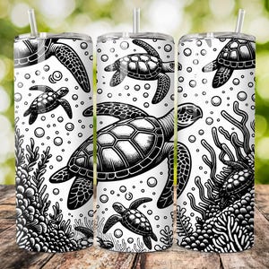 K&ouml;nnte beinhalten: Drei Edelstahlbecher mit einem schwarz-wei&szlig;en Design von Meeresschildkr&ouml;ten und Korallen. Die Becher stehen auf einer Holzoberfl&auml;che.
