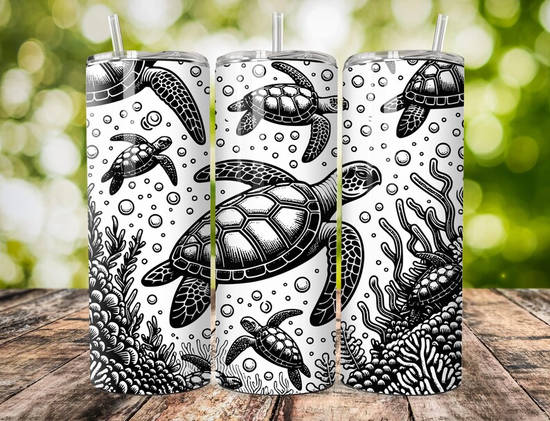 K&ouml;nnte beinhalten: Drei Edelstahlbecher mit einem schwarz-wei&szlig;en Design von Meeresschildkr&ouml;ten und Korallen. Die Becher stehen auf einer Holzoberfl&auml;che.