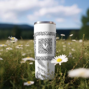 May include: White stainless steel tumbler with a black and white design of hearts and swirls. The design is centered on the tumbler and is surrounded by a border of hearts.