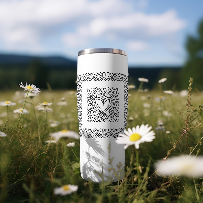 May include: White stainless steel tumbler with a black and white design of hearts and swirls. The design is centered on the tumbler and is surrounded by a border of hearts.