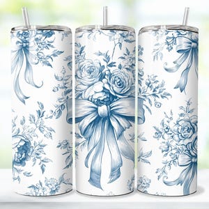 Op de afbeelding: Drie witte roestvrijstalen bekers met een blauw bloemen- en strikdesign. Elke beker heeft een zilveren deksel en een doorzichtige rietje. Het bloemenpatroon omvat rozen en andere bloemen.