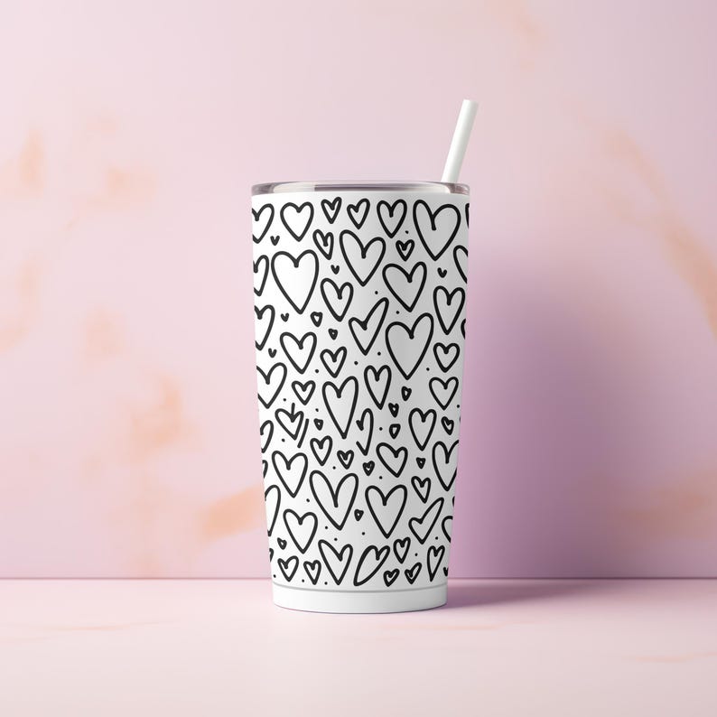 May include: White stainless steel tumbler with a black and white heart pattern. The tumbler has a straw.
