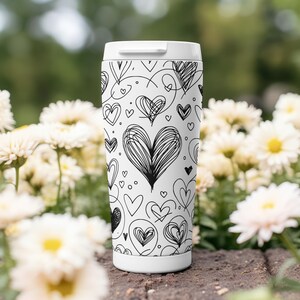 May include: White travel mug with a black and white pattern of hearts. The hearts are drawn in a variety of styles, some are simple and some are more intricate.