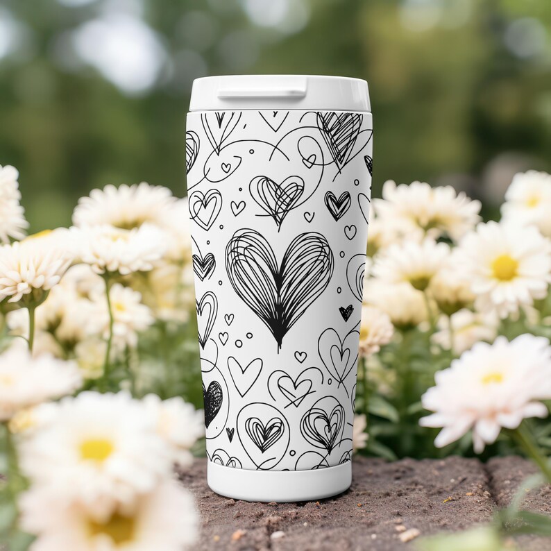 May include: White travel mug with a black and white pattern of hearts. The hearts are drawn in a variety of styles, some are simple and some are more intricate.