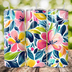 Puede incluir: Tres vasos aislados de acero inoxidable con diseños florales. Los vasos presentan un vibrante patrón de flores rosas, amarillas y naranjas con hojas azules y verdes sobre un fondo blanco. Cada vaso tiene una tapa transparente y una pajita.