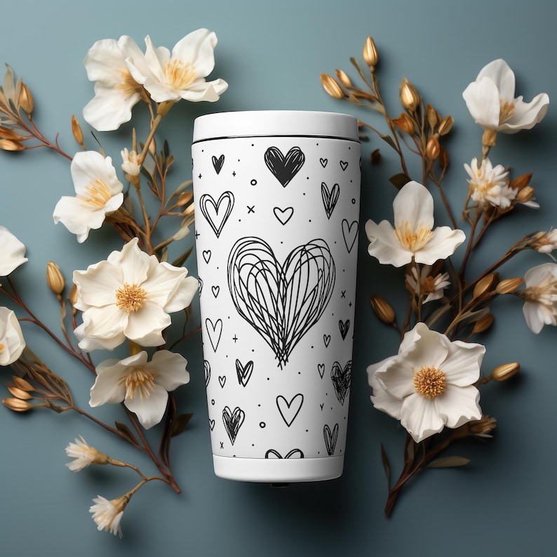 May include: White travel mug with a black and white heart pattern. The mug is surrounded by white flowers.