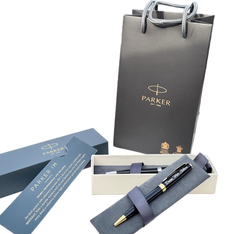May include: A black Parker IM ballpoint pen with gold accents and a personalized inscription in a gray pen case. The pen is in a black gift box with a gold Parker logo. The pen is also in a black shopping bag with a gold Parker logo.