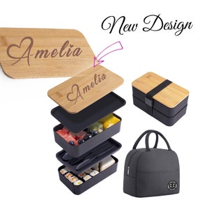 May include: A black and bamboo lunch box set with a personalised wooden lid that says "Amelia". The set includes a reusable lunch bag with a black fabric exterior and a zipper closure.