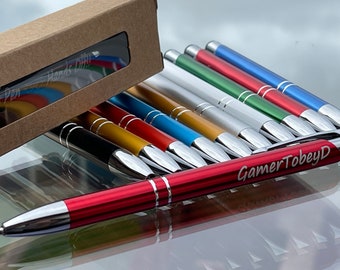 Pode incluir: Um conjunto de dez canetas coloridas com detalhes prateados e acabamento cromado. As canetas estão empilhadas, com a caneta superior apresentando o texto gravado "GamerTobeyD".