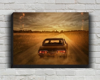 May include: A canvas print depicting a classic black car driving down a dirt road at sunset. The car is the focal point, kicking up dust as it moves towards the horizon. The sky is filled with warm orange and yellow hues.