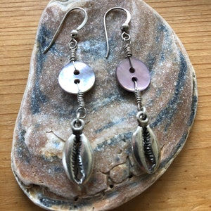 May include: A pair of silver earrings with a shell charm and a pink and white button charm.