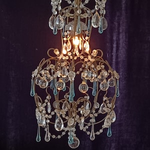 May include: A vintage chandelier with a gold metal frame and crystal drops. The chandelier has a teardrop shape and features blue and clear crystal accents.