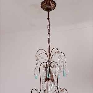 May include: A chandelier with a bronze finish and crystal drops. The chandelier has a decorative top with a scalloped edge. The crystal drops are clear and have a teardrop shape.