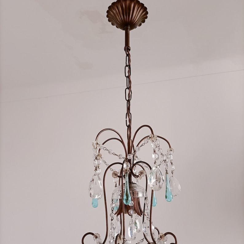 May include: A chandelier with a bronze finish and crystal drops. The chandelier has a decorative top with a scalloped edge. The crystal drops are clear and have a teardrop shape.