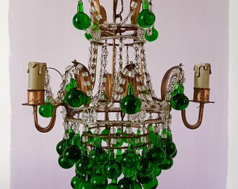 May include: A gold chandelier with green glass teardrop-shaped beads. The chandelier has a round, openwork design with a central ring and four arms. The arms are adorned with clear glass beads and the teardrop beads hang from the bottom of the chandelier.