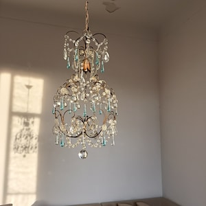 May include: A crystal chandelier with a gold metal frame and clear and blue glass crystals. The chandelier is hanging from the ceiling.