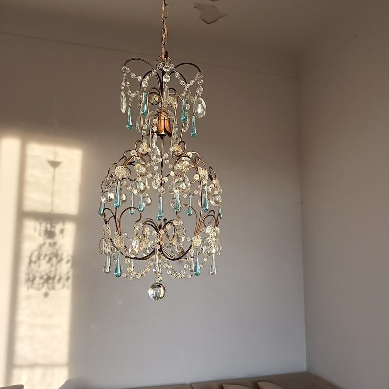 May include: A crystal chandelier with a gold metal frame and clear and blue glass crystals. The chandelier is hanging from the ceiling.