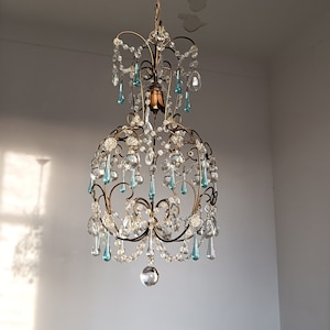 May include: A vintage chandelier with a gold metal frame and crystal drops. The chandelier has a teardrop shape and features blue and clear crystal accents.
