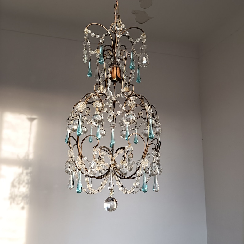May include: A vintage chandelier with a gold metal frame and crystal drops. The chandelier has a teardrop shape and features blue and clear crystal accents.