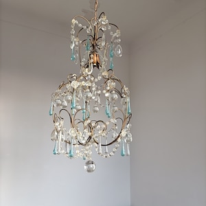 May include: A gold chandelier with crystal and blue glass drops. The chandelier has a round shape and is hanging from the ceiling.