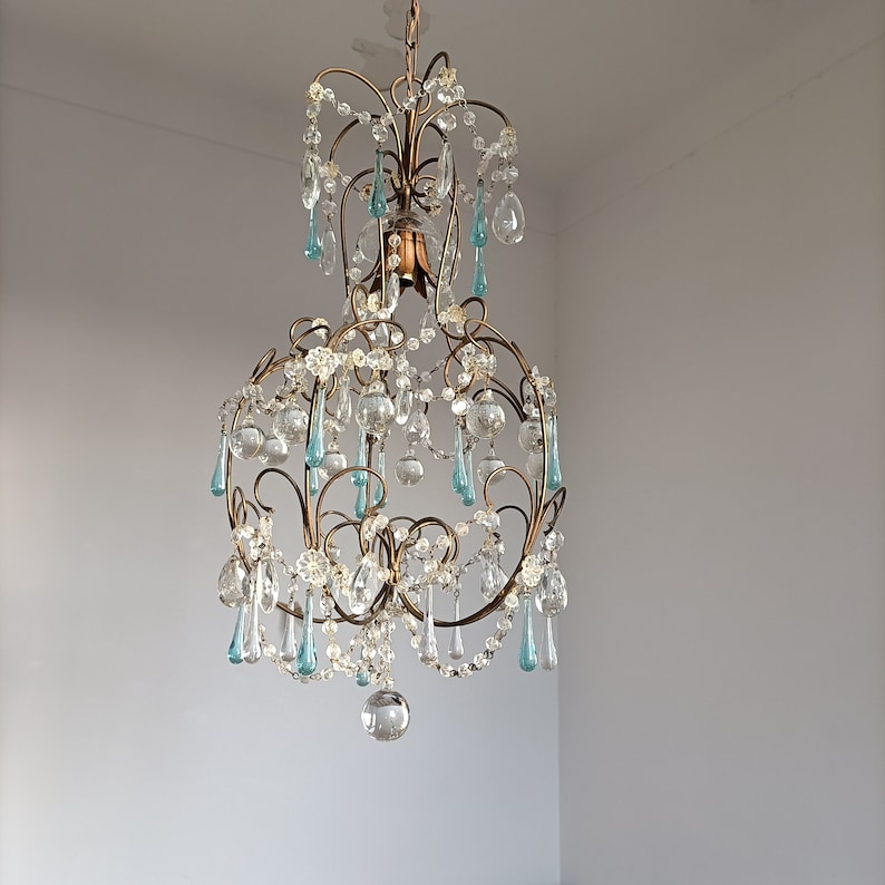 May include: A gold chandelier with crystal and blue glass drops. The chandelier has a round shape and is hanging from the ceiling.