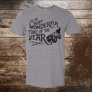 May include: A gray t-shirt with a black graphic of a jeep pulling a Christmas tree. The text on the shirt reads "It's the most wonderful time of the year."