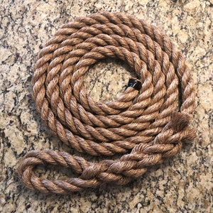 May include: A thick, natural brown rope coiled into a circle. The rope is made of natural fibers and has a rough texture. The rope is tied into a loop at one end.