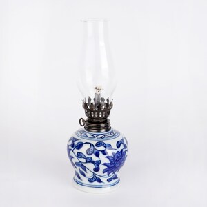 Puede incluir: Una l&aacute;mpara de aceite de porcelana azul y blanca con una chimenea de vidrio transparente. La l&aacute;mpara presenta un dise&ntilde;o floral.