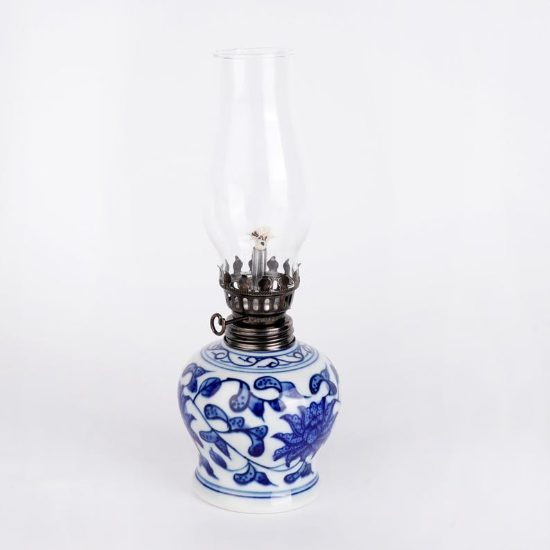 Puede incluir: Una l&aacute;mpara de aceite de porcelana azul y blanca con una chimenea de vidrio transparente. La l&aacute;mpara presenta un dise&ntilde;o floral.