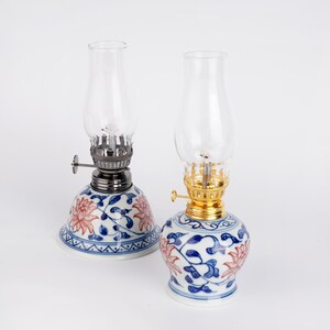 Puede incluir: Dos l&aacute;mparas de aceite de cer&aacute;mica azul y blanca con dise&ntilde;os florales. Las l&aacute;mparas tienen chimeneas de vidrio transparente y mechas de metal.